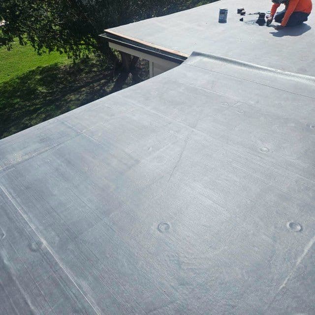 Flat roofing installation with gray materials and tools on a sunny day.
