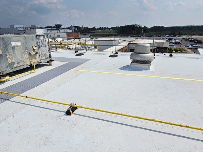 Industrial rooftop with ventilation units and safety railings under cloudy sky.