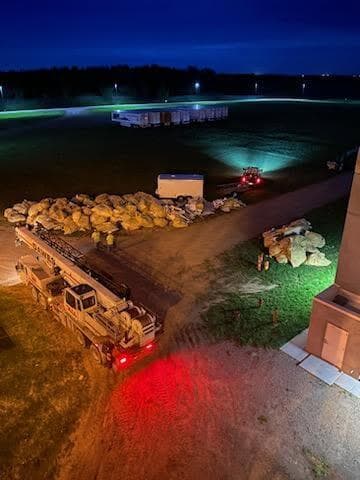 Fire truck and equipment illuminated at night near large piles of materials on a rural road.