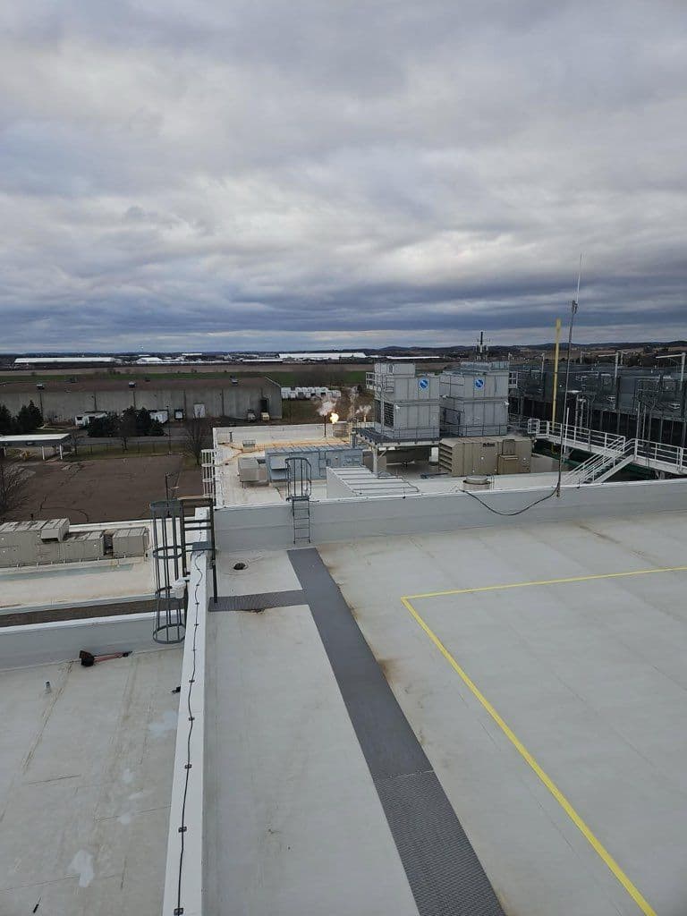 Rooftop view overlooking industrial buildings and cloudy sky with distant landscapes.